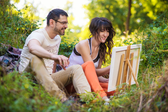 Couple Sitting At Outdoor Table Painting Landscape