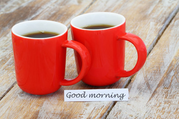 Good morning card with two red coffee mugs on rustic wooden surface
