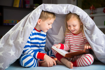 Happy siblings reading book under cover