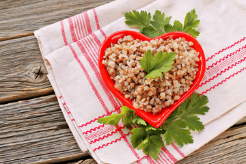 Heart plate with buckwheat porridge and parsley on napkin and wooden background