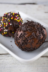 chocolate truffles with hundreds and thousands in a dish shot at an angle on white wooden boards