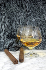 Two glasses of cognac with a cigar on a marble table