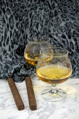 Two glasses of cognac with a cigar on a marble table