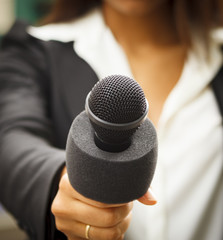 Close-up of a microphone being held by a female reoprter. Focus is on top of microphone.