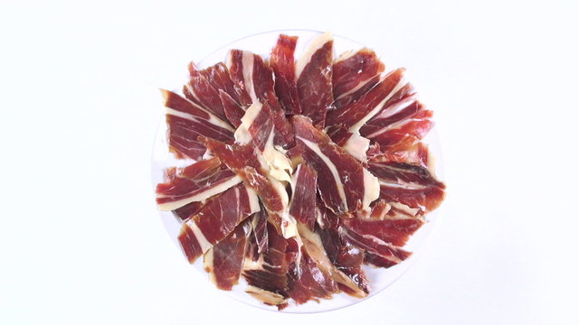 aerial top view of pile of typical spanish iberico ham sliced on dish rotating spinning on white background
