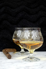 Two glasses of cognac with a cigar on a marble table