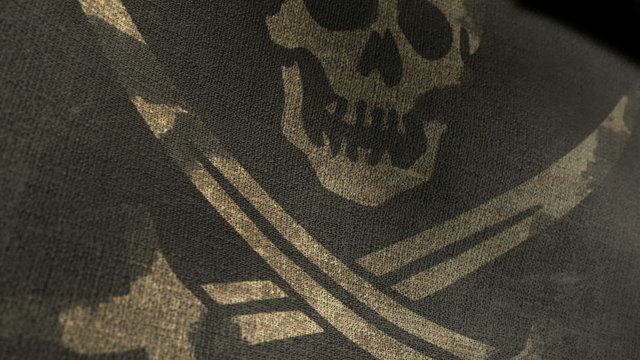 A regular jolly roger pirate flag with a skull and cutlasses on a black background attached to a wooden pole on a blue sky background