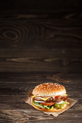 tasty Cheese burger with grilled meat, cheese, tomato, on craft paper on wooden surface. Fast food template. 