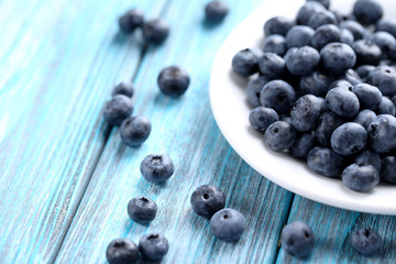 Tasty blueberries in plate on a blue wooden table