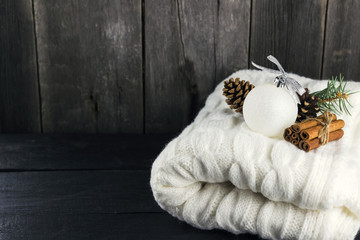 Knitted scarf, cinnamon, pine cones on a wooden background