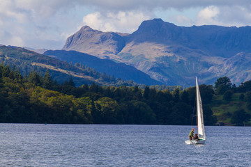 Fototapeta premium Sailboat in Lake Windermere, Cumbria, UK, with the forest and mountains in the background