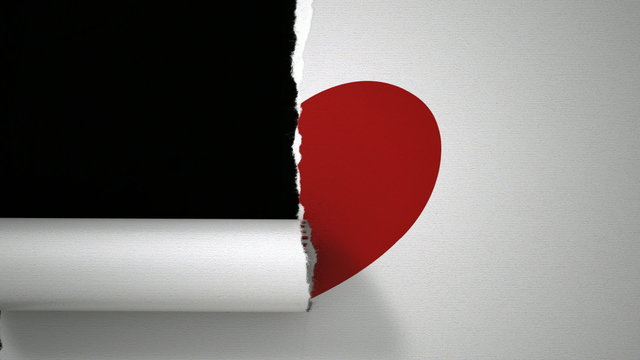 A closeup view of a white piece of paper tearing in two through a drawn red heart symbolising a broken heart