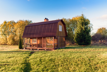 Small wooden house on a green field and trees on a background. 