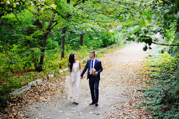 Fototapeta premium the bride and groom go hand against a background of green trees