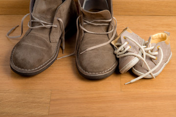 Closeup of father's shoes close to child's shoes on a parquet
