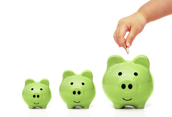 hand of a baby putting a golden coin into a green piggy bank with piles of golden coins arranged as a graph
