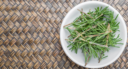 Fresh rosemary herbs over in white bowl over wicker background