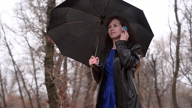 The woman in a black raincoat under an umbrella during a rain listens to music