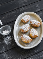 cookies madeleines with powdered sugar on oval plate on a light wooden surface