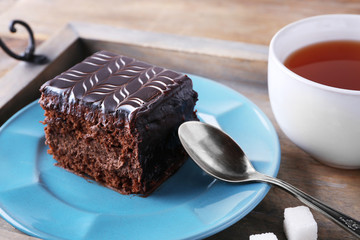 Sweet chocolate cake on blue plate with cup of tea on wooden tray