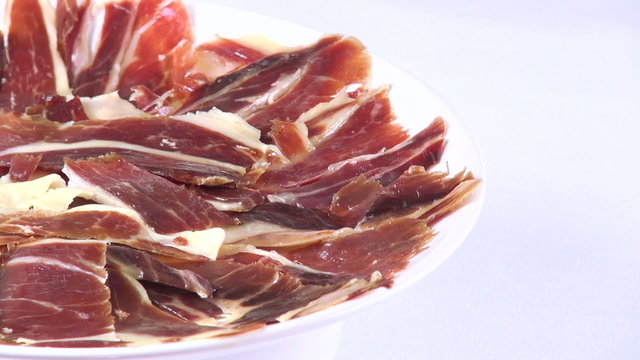 view of pile of typical spanish iberico ham sliced on dish rotating spinning on white background
