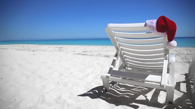 Santa Claus Hat on sunbed near  tropical calm beach with turquoise caribbean sea water and white sand. Christmas vacation concept