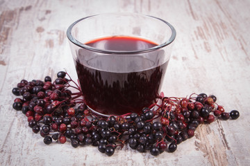 Bunch of fresh elderberry with juice on old wooden background, healthy nutrition