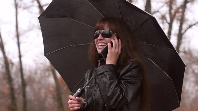 The woman the superhero in the rain with a black umbrella calls by telephone