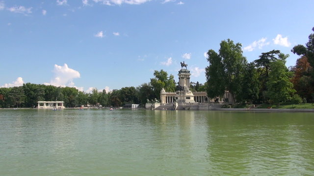 landmark with big green water pond in Retiro urban park with sculpture monument and people rowing boats in Madrid city Spain Europe
