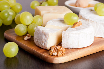 cheeses, grapes and walnuts on a wooden background, horizontal