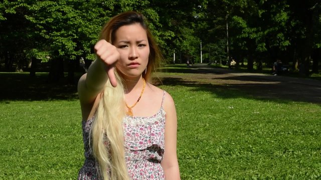 young attractive asian woman shows thumb down in the park 