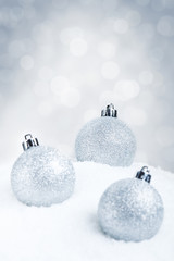 Silver Christmas baubles on snow with a silver background
