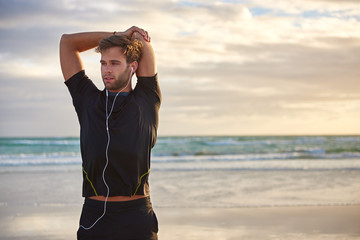 Man with earphones stretching on the beach in the morning