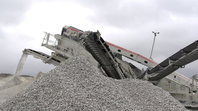 A gravel crusher with some stones falling on the ground. Usint the splinter gravel crusher crushes the big stones into gravels