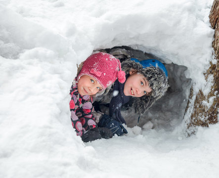Happy boy and girl looking out from a snow cave they made in a snowdrift