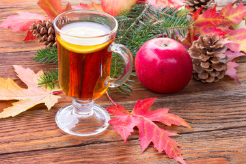 tea with cinnamon and lemon, ripe apples, red autumn maple leaves, fir branch and pine cones on...