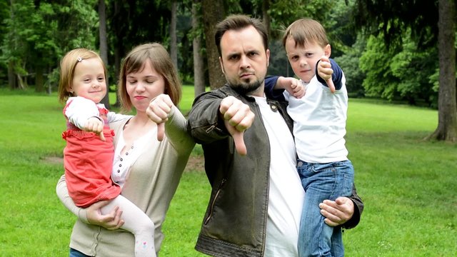 family (middle couple in love, cute girl and small boy) show thumb on disagreement in the park