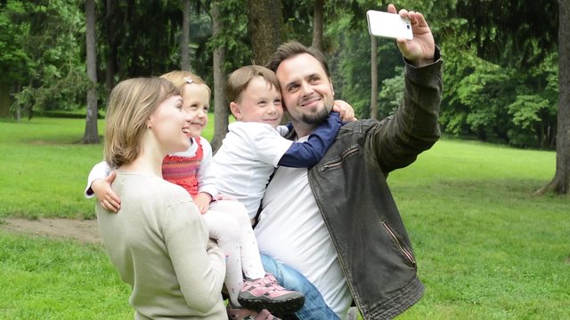 family (middle couple in love, cute girl and small boy) take a photo with smartphone (selfie) - park