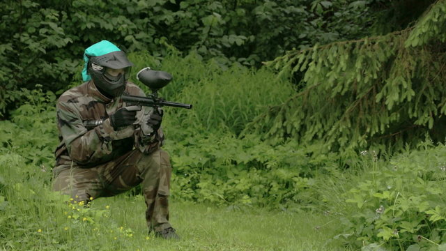 A man in blue cap playing the paintball. Paintball is a sport in which players compete in teams or individually to eliminate opponents by tagging them with capsules containing water-soluble dye 