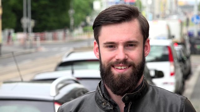 young handsome hipster man smiles to camera - city: urban street with passing cars - closeup