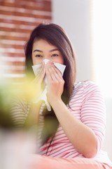 Asian woman blowing her nose on couch