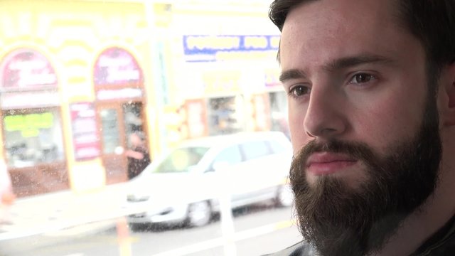 young handsome hipster man travel by tram and looks out of the window - street with people - closeup