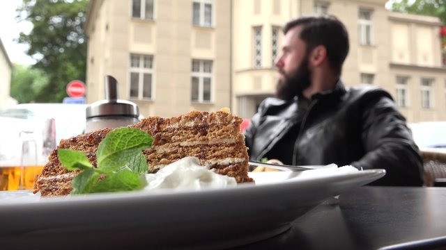 food - dessert - honey cake - young handsome man (hipster) sitting in background - restaurant outdoor seating