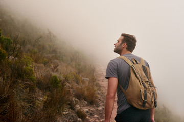 Young hiker looking up at a misty mountain side