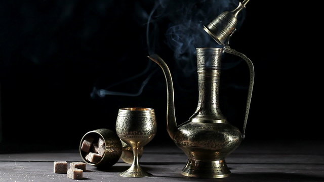 Metal pot and cup with moroccan tea and smoke at black bacground