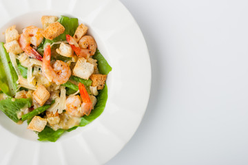 Caesar salad with prawns on the white plate top view
