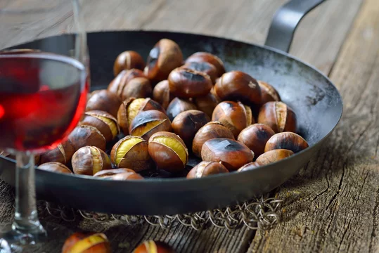 Pfanne mit frisch gerösteten Maronen. mit einem Glas Vernatsch zum Törggelen in Südtirol serviert