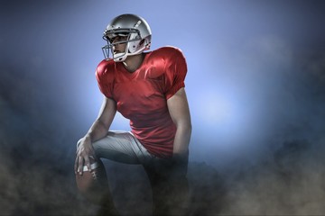 Sportsman holding american football while kneeling