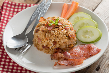 Fried rice with bacon and vegetables on wood table.