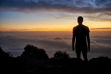 Silhouette of a man on a mountain with a  cloudy sunrise